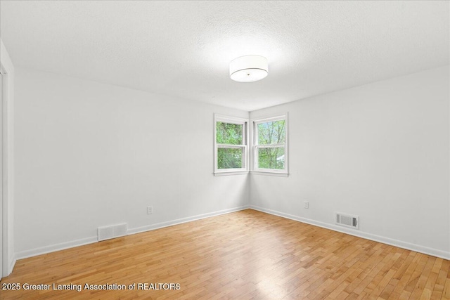 spare room featuring light wood finished floors, baseboards, and visible vents