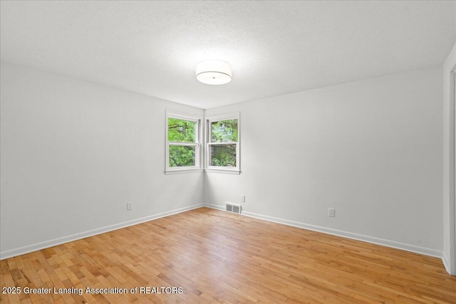 unfurnished room featuring baseboards, visible vents, light wood-type flooring, and a textured ceiling