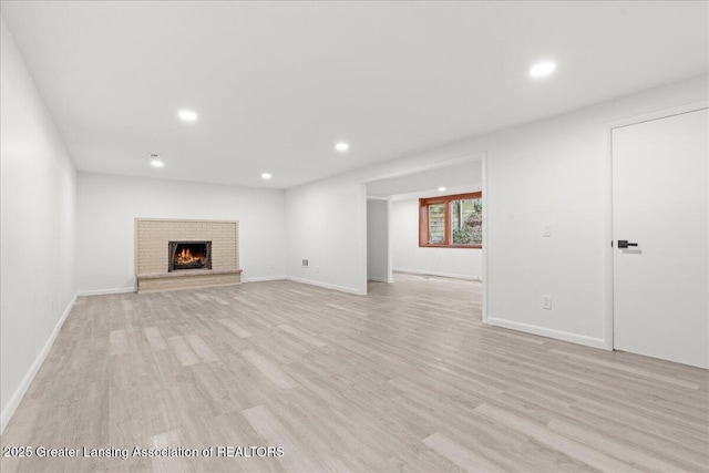 unfurnished living room featuring baseboards, a brick fireplace, light wood finished floors, and recessed lighting