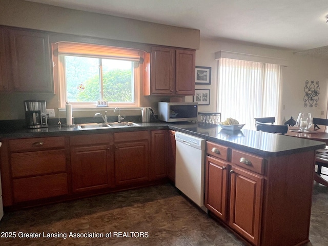 kitchen featuring stainless steel microwave, a sink, dishwasher, a peninsula, and dark countertops