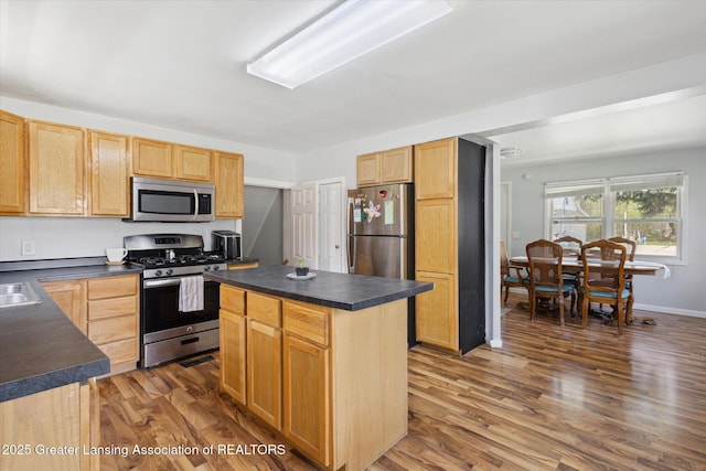 kitchen featuring dark countertops, stainless steel appliances, light brown cabinets, and wood finished floors