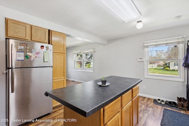 kitchen featuring wood finished floors, freestanding refrigerator, baseboards, a kitchen island, and dark countertops