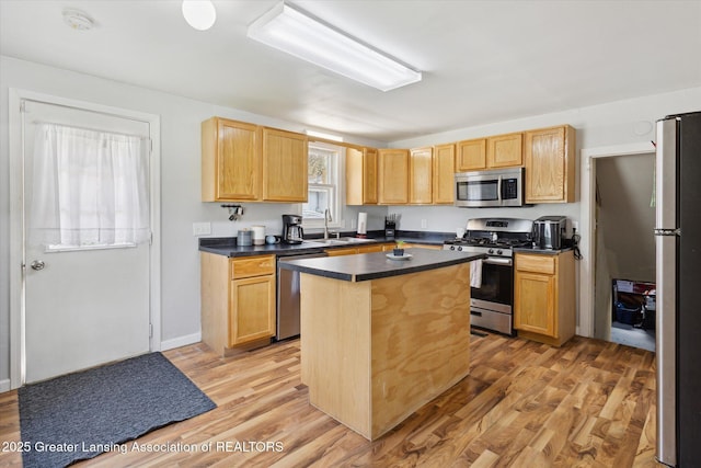 kitchen featuring a sink, light wood-style flooring, a center island, dark countertops, and appliances with stainless steel finishes