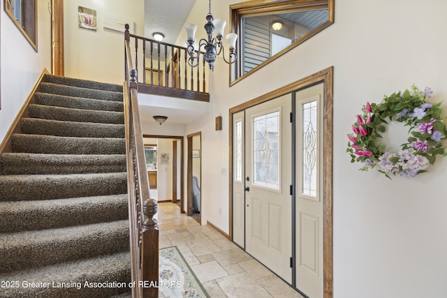 foyer entrance featuring stone tile flooring, stairs, baseboards, a chandelier, and a towering ceiling