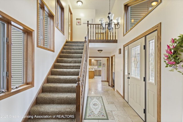 entrance foyer with a chandelier, stone tile floors, stairs, baseboards, and a towering ceiling