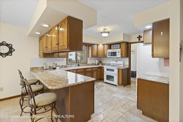kitchen with white appliances, a peninsula, a textured ceiling, brown cabinetry, and a kitchen bar