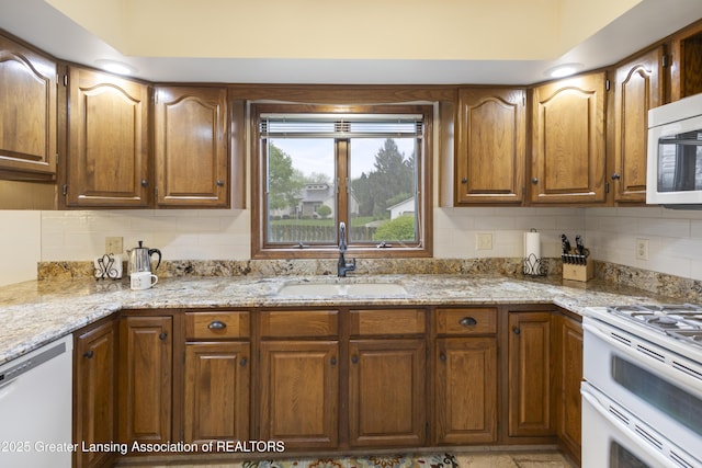 kitchen with a sink, white appliances, decorative backsplash, and light stone countertops