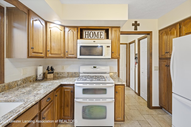 kitchen with white appliances, stone tile floors, backsplash, and brown cabinetry