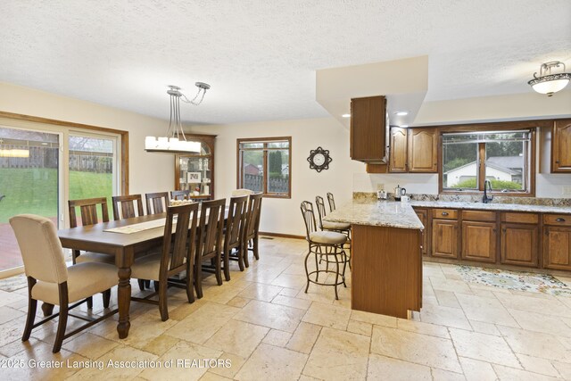 kitchen featuring brown cabinets, stone tile flooring, a peninsula, plenty of natural light, and a textured ceiling