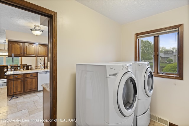 laundry area featuring washer and clothes dryer, a textured ceiling, stone tile flooring, and baseboards