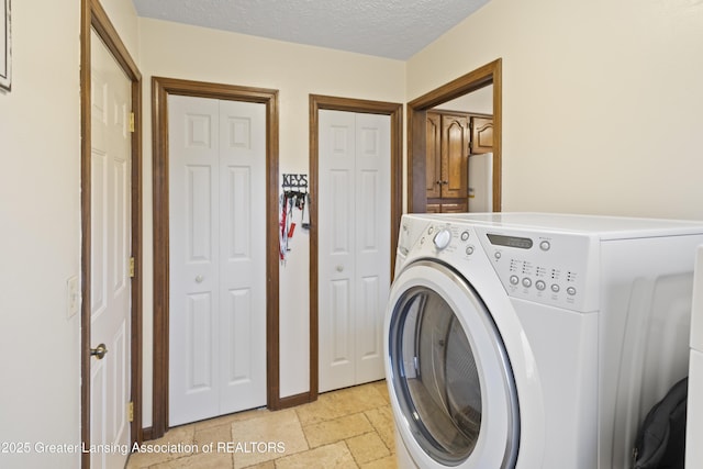 laundry area featuring washer / clothes dryer, cabinet space, stone tile floors, and a textured ceiling