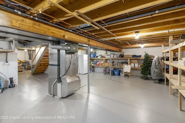 unfinished below grade area featuring freestanding refrigerator, stairs, and heating unit