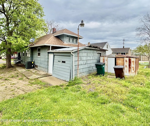 rear view of property featuring a chimney, an outbuilding, central air condition unit, roof with shingles, and a storage unit
