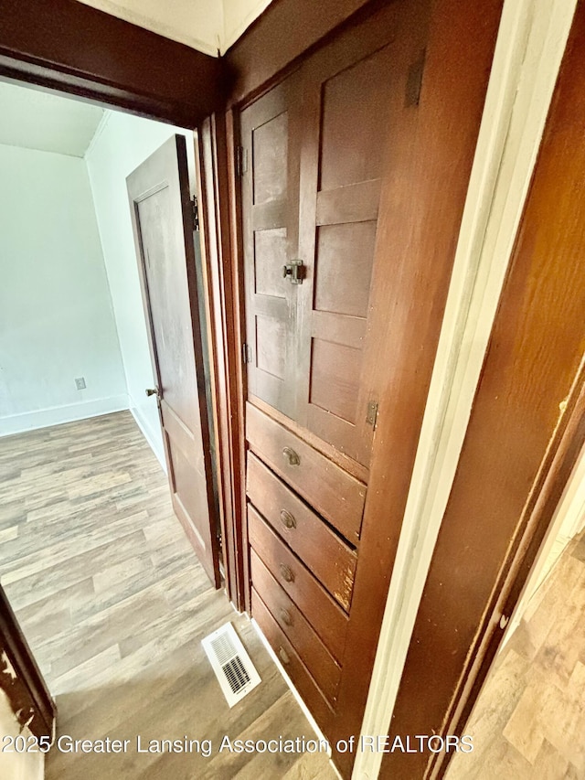 hall featuring baseboards, light wood-type flooring, and visible vents