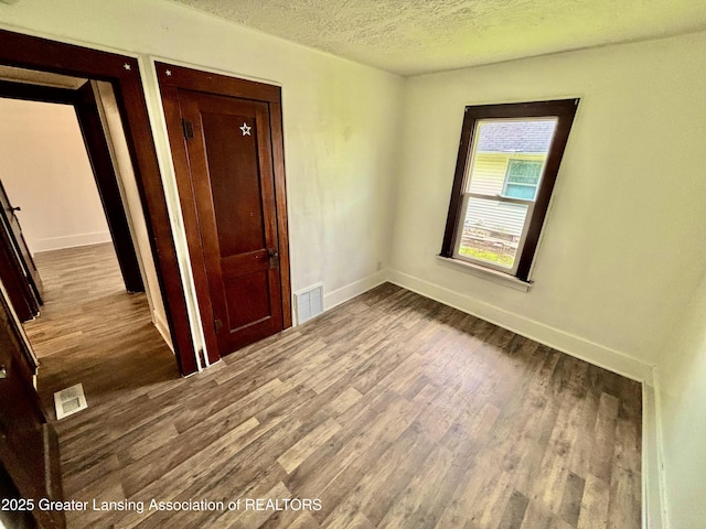 unfurnished bedroom featuring a textured ceiling, visible vents, wood finished floors, and baseboards