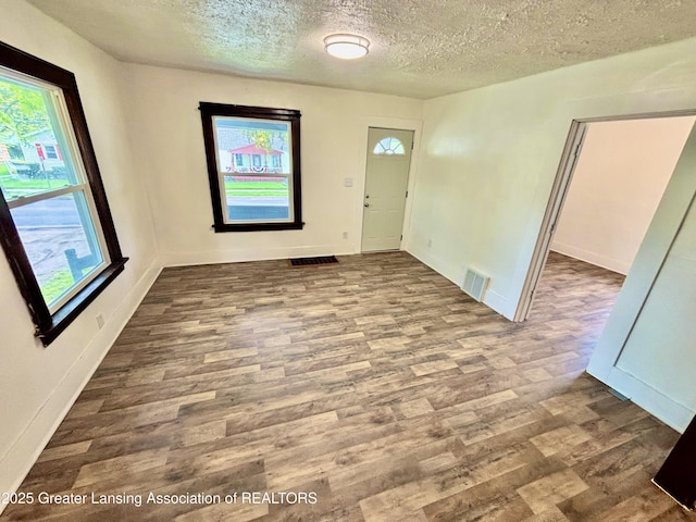 interior space with a textured ceiling, baseboards, visible vents, and wood finished floors