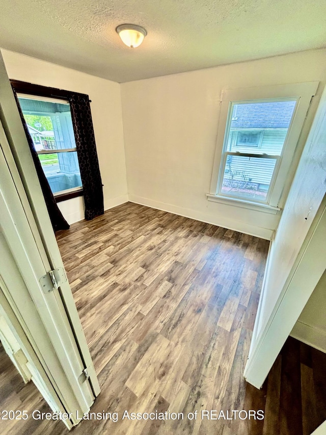 spare room with a textured ceiling, baseboards, and wood finished floors
