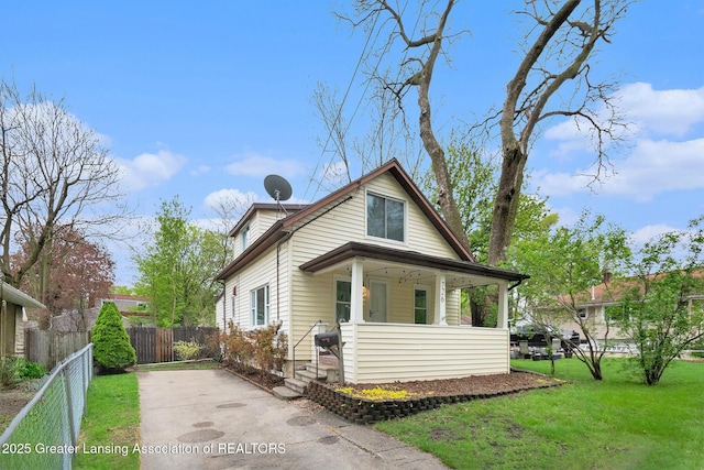 view of front facade with a front lawn, a porch, driveway, and fence