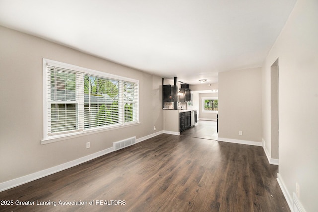 unfurnished living room featuring dark wood-style flooring, a wealth of natural light, baseboards, and visible vents