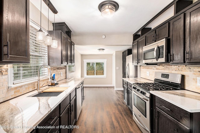 kitchen featuring light stone counters, a sink, dark brown cabinetry, tasteful backsplash, and appliances with stainless steel finishes