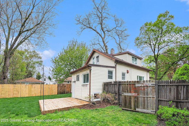 back of property featuring a yard, a chimney, a wooden deck, and a fenced backyard