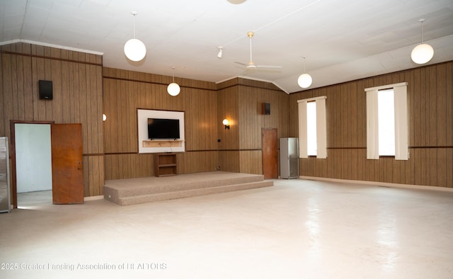 unfurnished living room featuring vaulted ceiling, wooden walls, and a ceiling fan