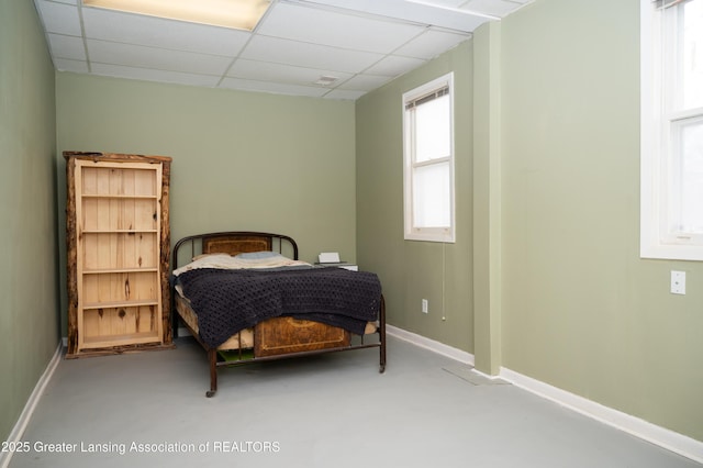 bedroom with a drop ceiling, finished concrete flooring, and baseboards