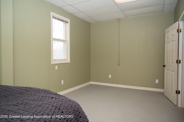 bedroom with a drop ceiling, baseboards, and finished concrete floors
