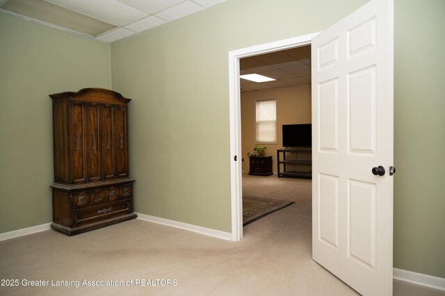 corridor featuring a drop ceiling, light carpet, and baseboards