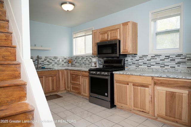 kitchen featuring stainless steel appliances, a sink, light brown cabinetry, tasteful backsplash, and light stone counters