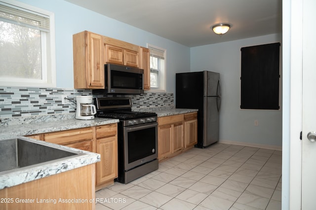kitchen with appliances with stainless steel finishes, decorative backsplash, a sink, and light brown cabinetry