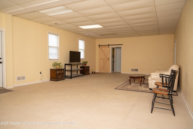 living area featuring a barn door, a drop ceiling, baseboards, and carpet