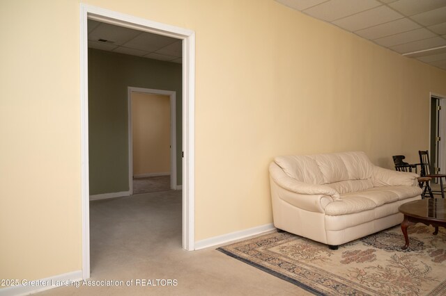 living area featuring carpet floors, a paneled ceiling, and baseboards