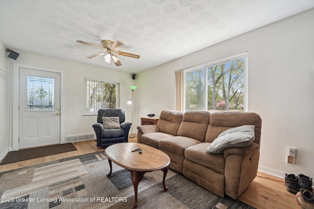 living area featuring healthy amount of natural light, wood finished floors, ceiling fan, baseboards, and a textured ceiling