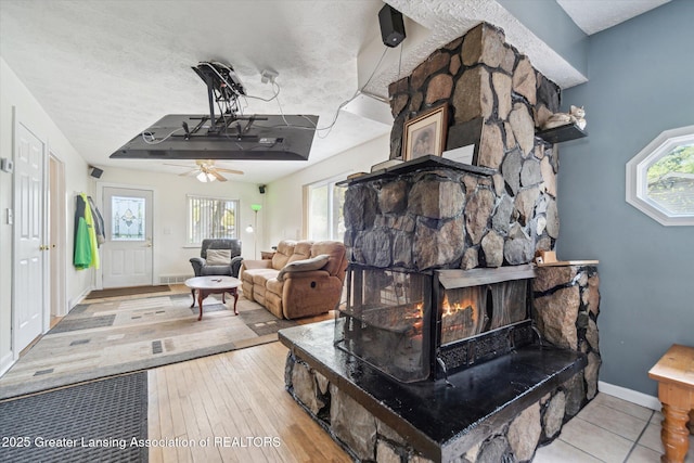 living room with baseboards, a ceiling fan, a stone fireplace, and hardwood / wood-style floors