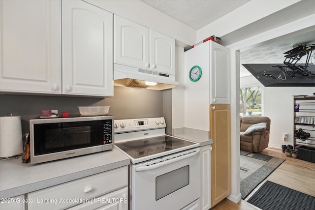 kitchen featuring stainless steel microwave, white electric range, under cabinet range hood, white cabinetry, and a textured ceiling