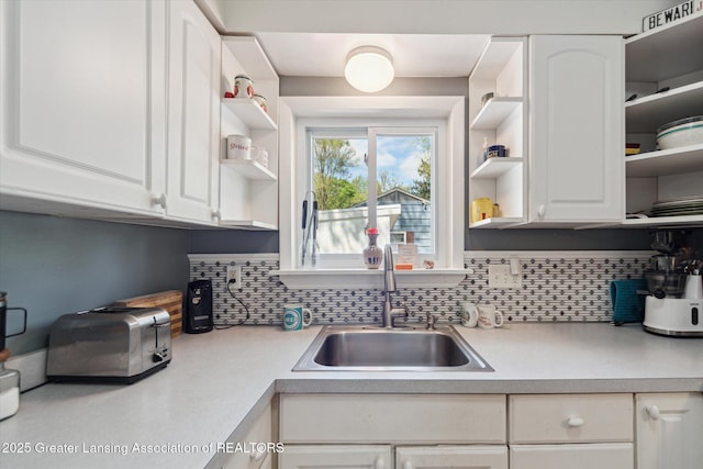 kitchen with open shelves, a sink, white cabinets, backsplash, and light countertops