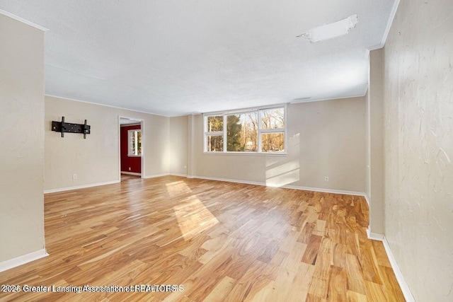 spare room with light wood-style flooring, ornamental molding, and baseboards