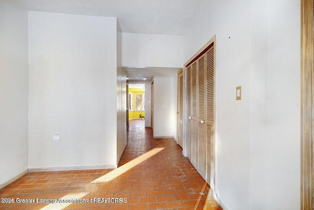 hallway featuring brick floors and baseboards