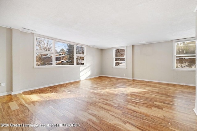 empty room with wood finished floors, healthy amount of natural light, and baseboards
