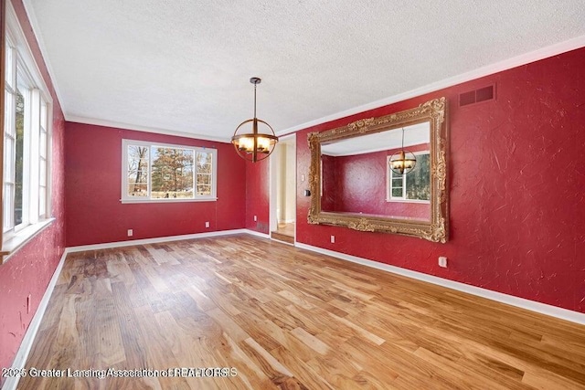 unfurnished dining area with a textured ceiling, wood finished floors, a chandelier, a textured wall, and crown molding
