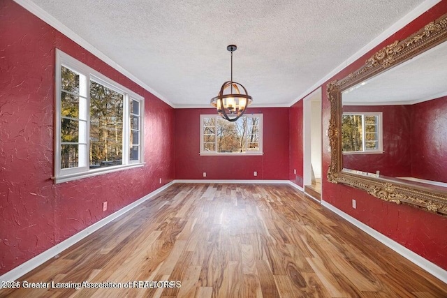 unfurnished dining area with ornamental molding, wood finished floors, healthy amount of natural light, a textured ceiling, and baseboards