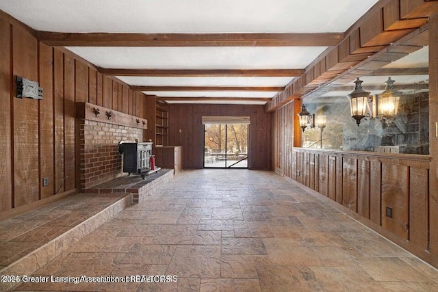 unfurnished living room with a wood stove, stone tile flooring, wooden walls, beamed ceiling, and a chandelier