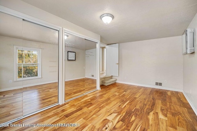 unfurnished bedroom with wood finished floors, two closets, a textured ceiling, and baseboards