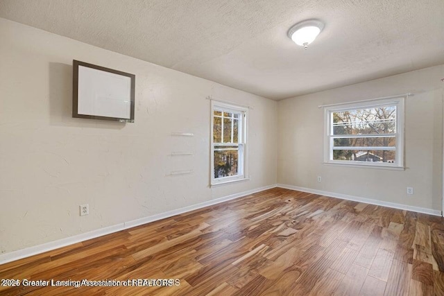 empty room with a textured ceiling, wood finished floors, healthy amount of natural light, and baseboards