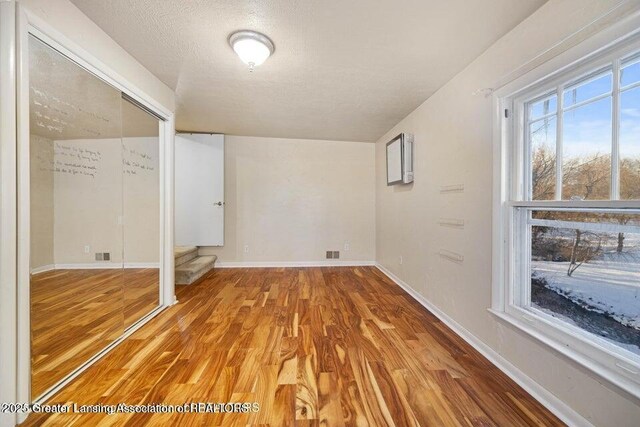 basement featuring light wood-style flooring, baseboards, and a textured ceiling