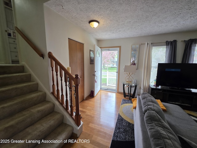 living room featuring stairway, light wood-style floors, and a textured ceiling