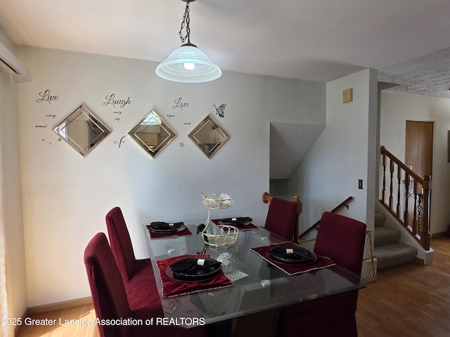 dining room with wood finished floors, stairs, an AC wall unit, and baseboards