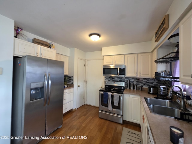 kitchen featuring appliances with stainless steel finishes, a sink, backsplash, dark wood finished floors, and white cabinets