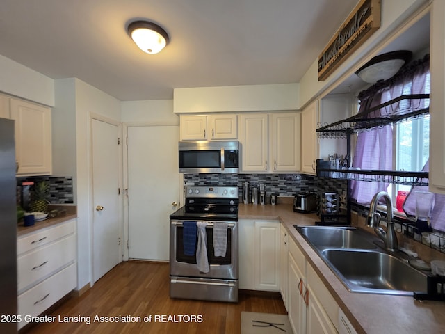kitchen with appliances with stainless steel finishes, a sink, tasteful backsplash, white cabinets, and dark wood-type flooring